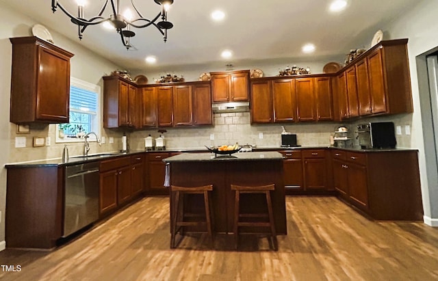 kitchen featuring dishwasher, dark countertops, a sink, and under cabinet range hood