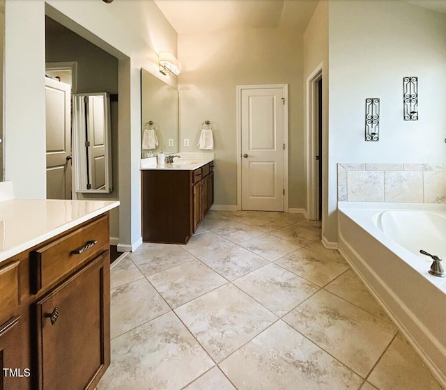 bathroom with a garden tub, two vanities, a sink, and baseboards