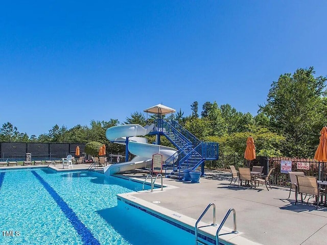 community pool with a patio, a water slide, and fence