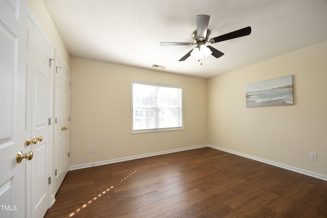 unfurnished bedroom featuring visible vents, dark wood finished floors, a textured ceiling, and baseboards