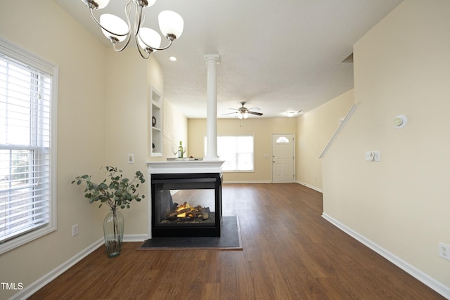 unfurnished living room featuring ornate columns, wood finished floors, a multi sided fireplace, and baseboards