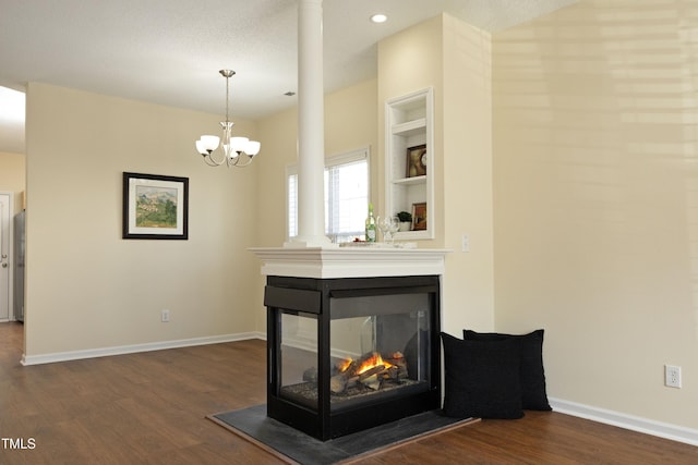 unfurnished living room with built in shelves, dark wood-type flooring, a multi sided fireplace, a chandelier, and baseboards