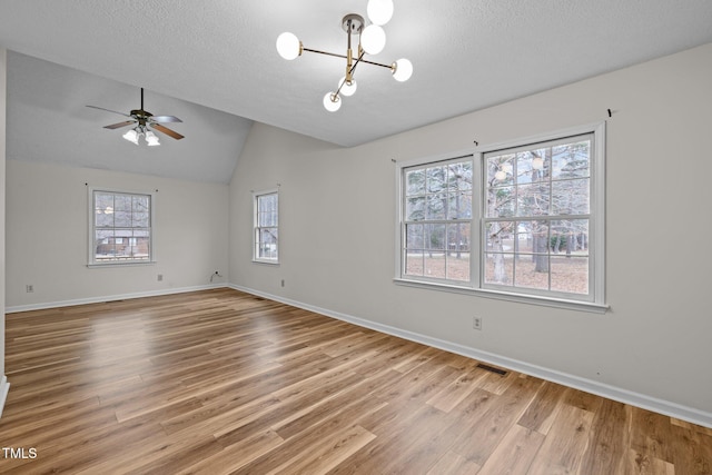 unfurnished room featuring lofted ceiling, a textured ceiling, wood finished floors, and visible vents