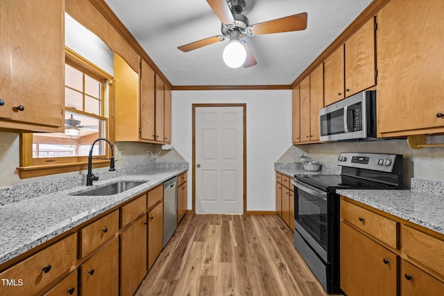 kitchen featuring light wood-style flooring, brown cabinets, stainless steel appliances, crown molding, and a sink