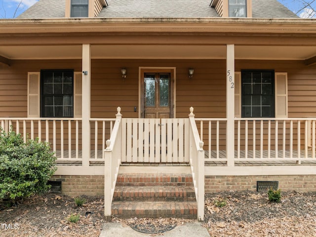 view of exterior entry with roof with shingles, a porch, and crawl space