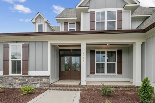 view of exterior entry featuring french doors, board and batten siding, a shingled roof, and stone siding