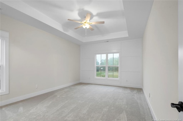 spare room featuring a tray ceiling, light colored carpet, ceiling fan, and baseboards