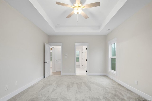 unfurnished bedroom with a raised ceiling, light carpet, baseboards, and multiple windows