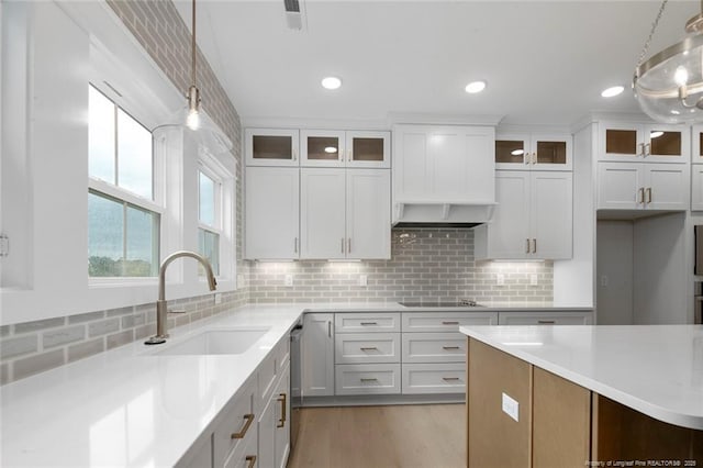 kitchen featuring black electric stovetop, light countertops, backsplash, decorative light fixtures, and a sink