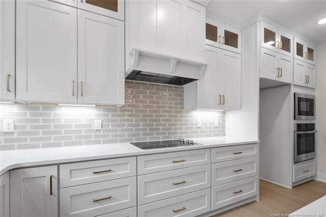 kitchen with premium range hood, light countertops, backsplash, white cabinetry, and appliances with stainless steel finishes