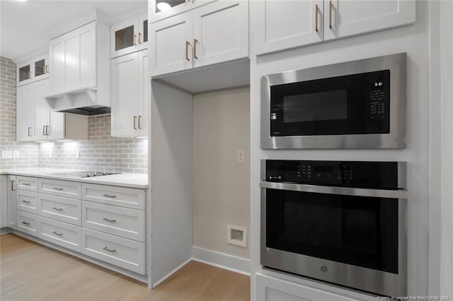 kitchen with stainless steel oven, light wood-style flooring, tasteful backsplash, black electric stovetop, and built in microwave