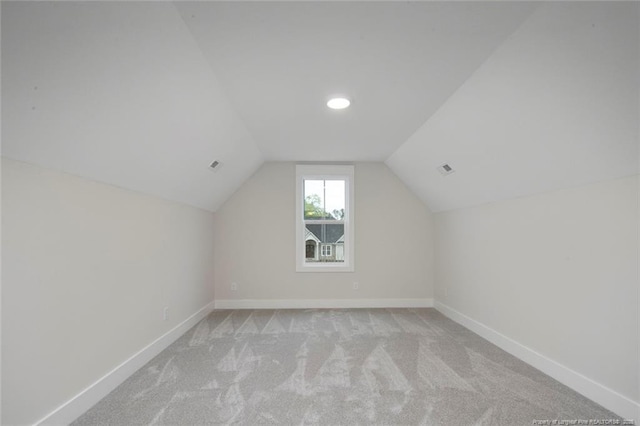additional living space with visible vents, baseboards, vaulted ceiling, and light carpet