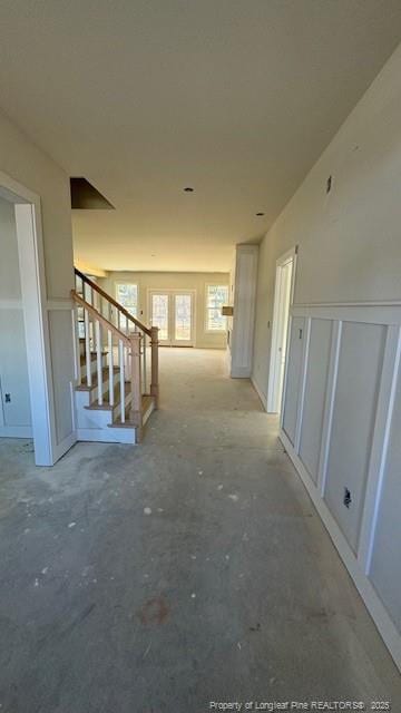 corridor featuring stairs, wainscoting, and a decorative wall