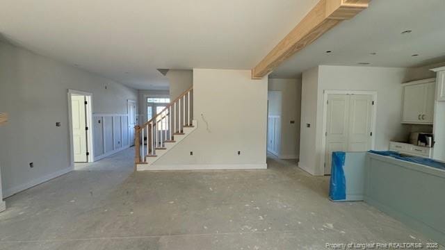 unfurnished living room featuring stairway and baseboards