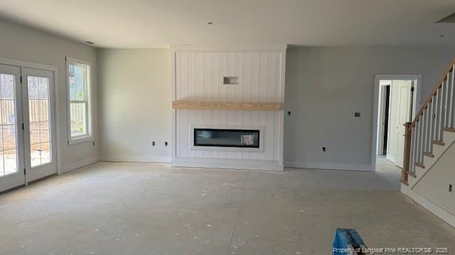 unfurnished living room featuring stairs, a large fireplace, baseboards, and unfinished concrete floors