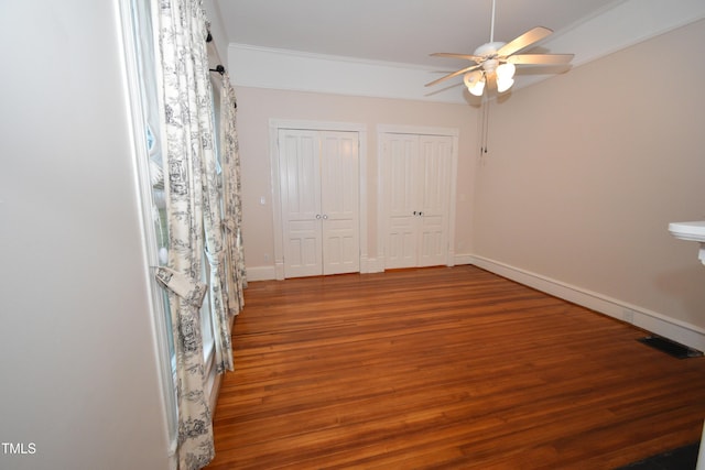 unfurnished bedroom featuring wood finished floors, visible vents, baseboards, two closets, and crown molding