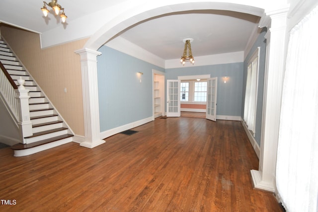 empty room featuring arched walkways, visible vents, stairway, wood finished floors, and ornate columns