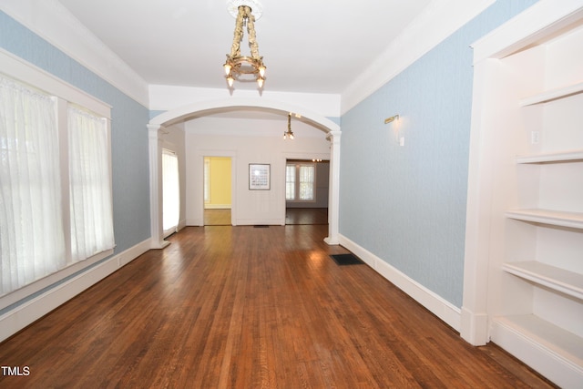 empty room with ornate columns, built in shelves, arched walkways, and wood finished floors