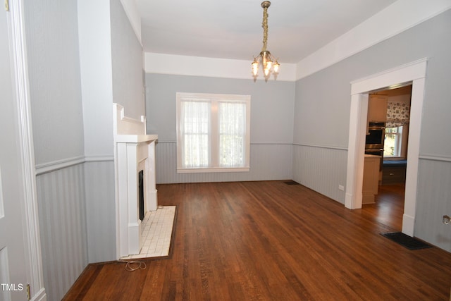 unfurnished living room featuring visible vents, wainscoting, wood finished floors, a fireplace, and a chandelier