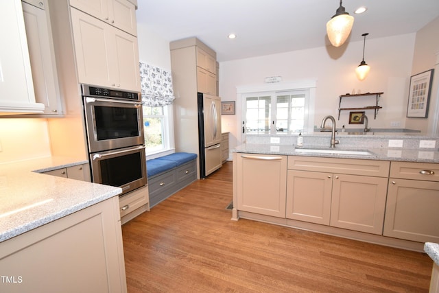 kitchen featuring a sink, light wood-style floors, appliances with stainless steel finishes, light stone countertops, and decorative light fixtures