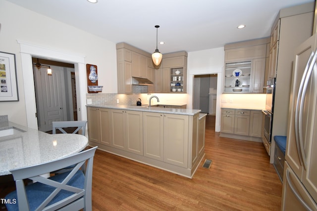 kitchen with light wood-style floors, visible vents, under cabinet range hood, and decorative backsplash