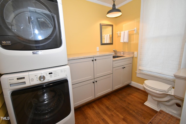 clothes washing area featuring dark wood finished floors, crown molding, stacked washer / drying machine, a sink, and laundry area