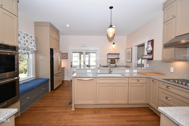 kitchen featuring tasteful backsplash, appliances with stainless steel finishes, light wood-style floors, a sink, and a peninsula