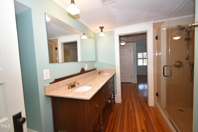 bathroom with wood finished floors, a sink, visible vents, double vanity, and a stall shower