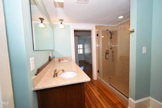 bathroom featuring wood finished floors, a sink, double vanity, a stall shower, and crown molding