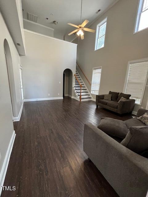 unfurnished living room featuring arched walkways, plenty of natural light, stairway, and wood finished floors