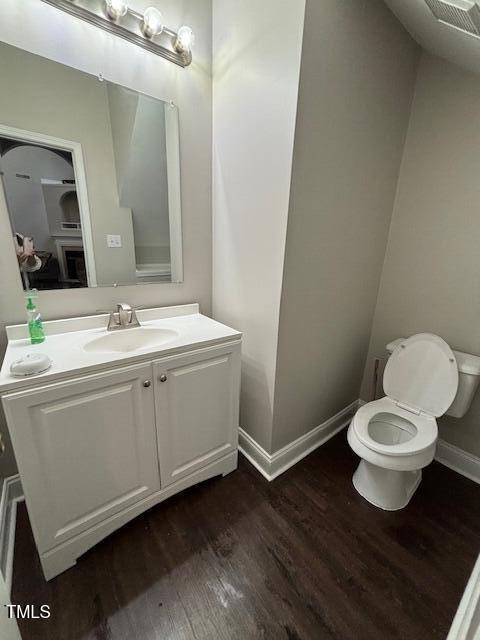 half bath with baseboards, vanity, toilet, and wood finished floors