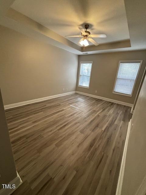 empty room with a ceiling fan, baseboards, a tray ceiling, and wood finished floors