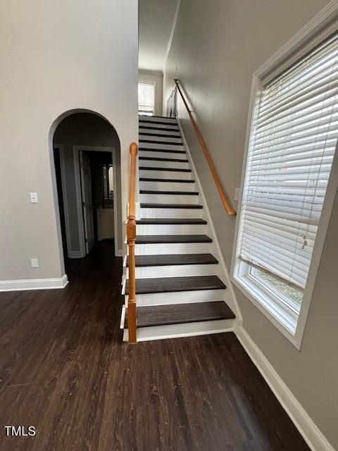 stairway with arched walkways, wood finished floors, and baseboards