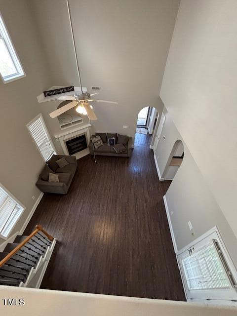 unfurnished living room with arched walkways, ceiling fan, a fireplace, wood finished floors, and baseboards