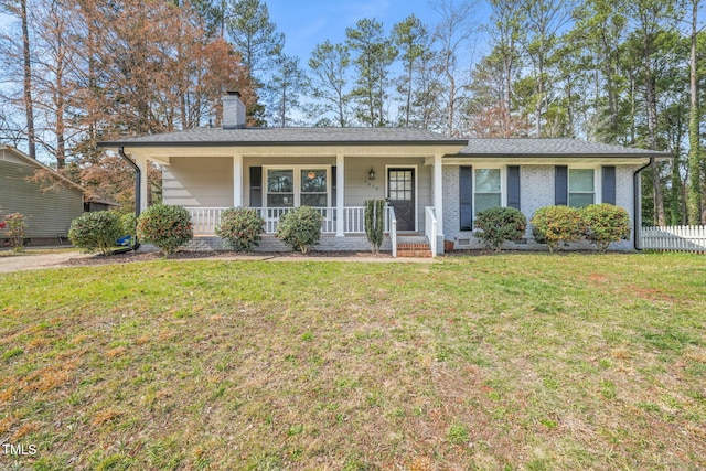 ranch-style home featuring a shingled roof, a chimney, covered porch, a front yard, and brick siding