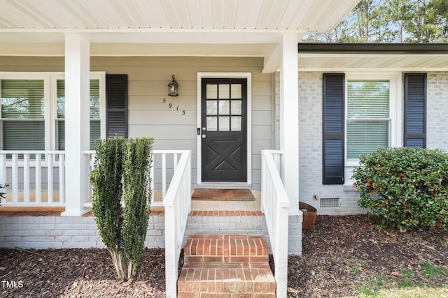 view of exterior entry with covered porch, brick siding, and crawl space