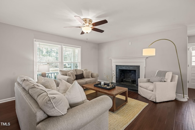 living room with ceiling fan, baseboards, a fireplace with raised hearth, and dark wood-style flooring