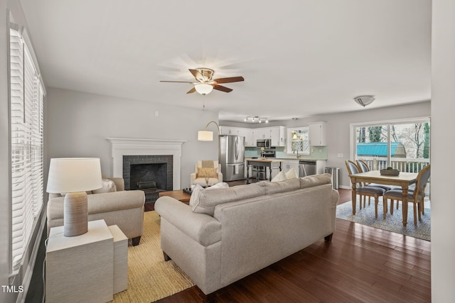 living room with ceiling fan, dark wood-type flooring, and a brick fireplace