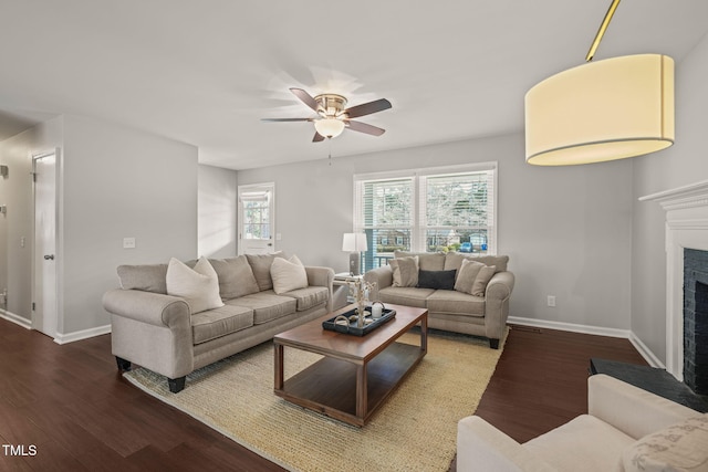 living room with a ceiling fan, baseboards, a fireplace with raised hearth, and wood finished floors