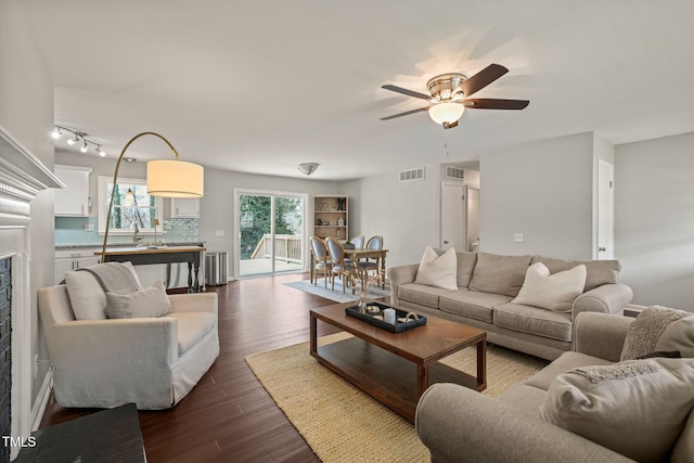 living room with a ceiling fan, visible vents, and dark wood-type flooring