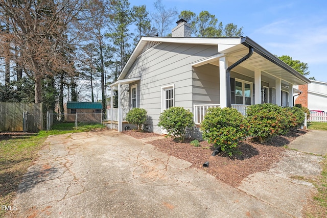 view of side of property with covered porch, a chimney, and fence