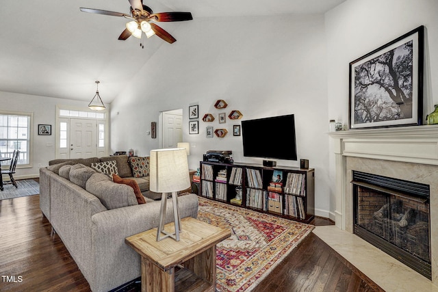 living area featuring high vaulted ceiling, a ceiling fan, wood finished floors, a fireplace, and baseboards