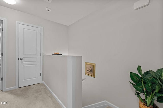 hall featuring light carpet, an upstairs landing, and baseboards