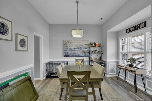 dining space featuring a wainscoted wall, wood finished floors, visible vents, and a decorative wall