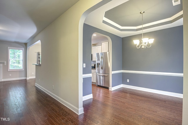 spare room featuring visible vents, baseboards, dark wood finished floors, a raised ceiling, and a chandelier