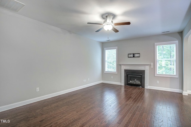 unfurnished living room featuring dark wood-style flooring, visible vents, a ceiling fan, a glass covered fireplace, and baseboards