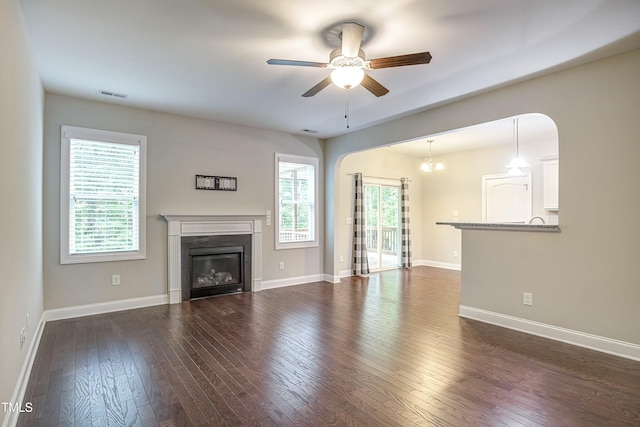 unfurnished living room featuring a wealth of natural light, visible vents, dark wood finished floors, and a glass covered fireplace