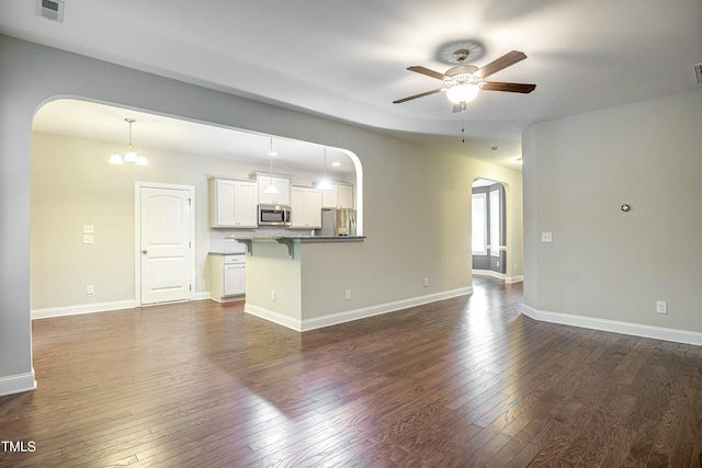 unfurnished living room featuring arched walkways, dark wood-style flooring, visible vents, and ceiling fan with notable chandelier