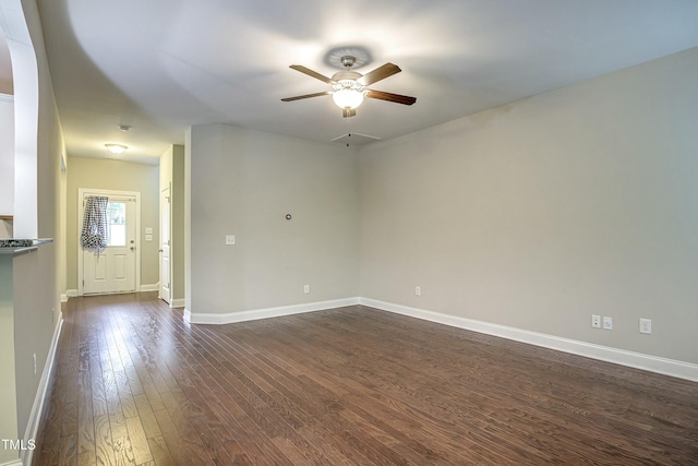 spare room with dark wood-style flooring, a ceiling fan, and baseboards