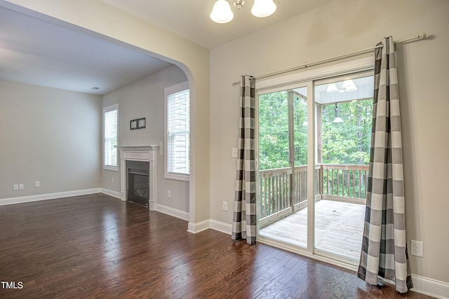 interior space with arched walkways, baseboards, a glass covered fireplace, and dark wood-style floors